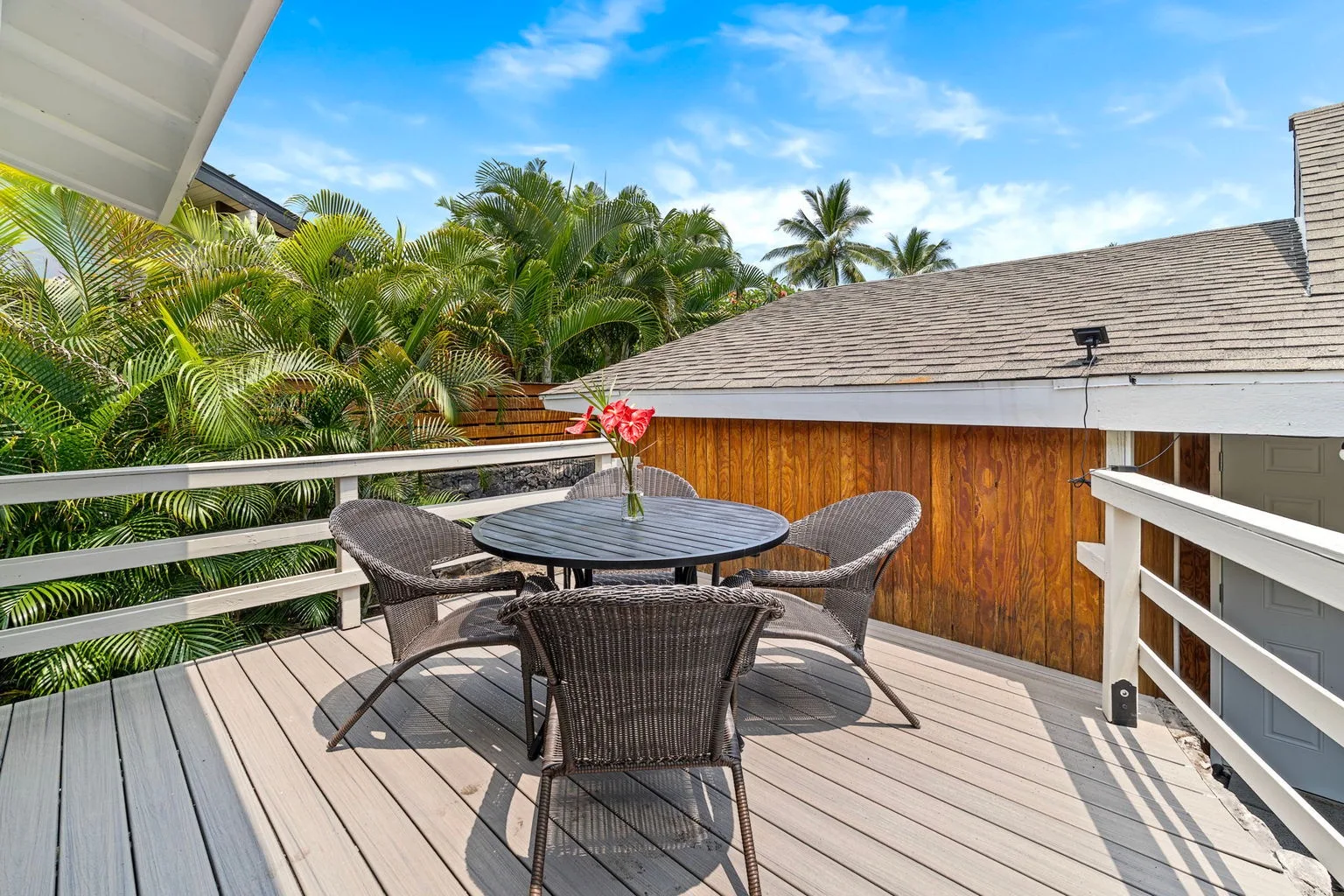 A deck seating area with a round table overlooks palm trees and a wooden building.