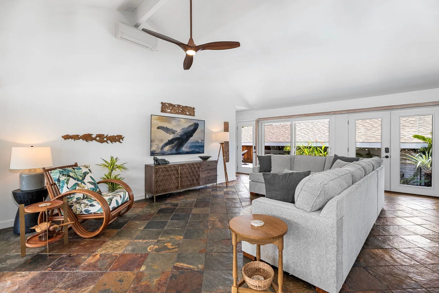 A bright living room has a gray seating area and large windows overlooking greenery.