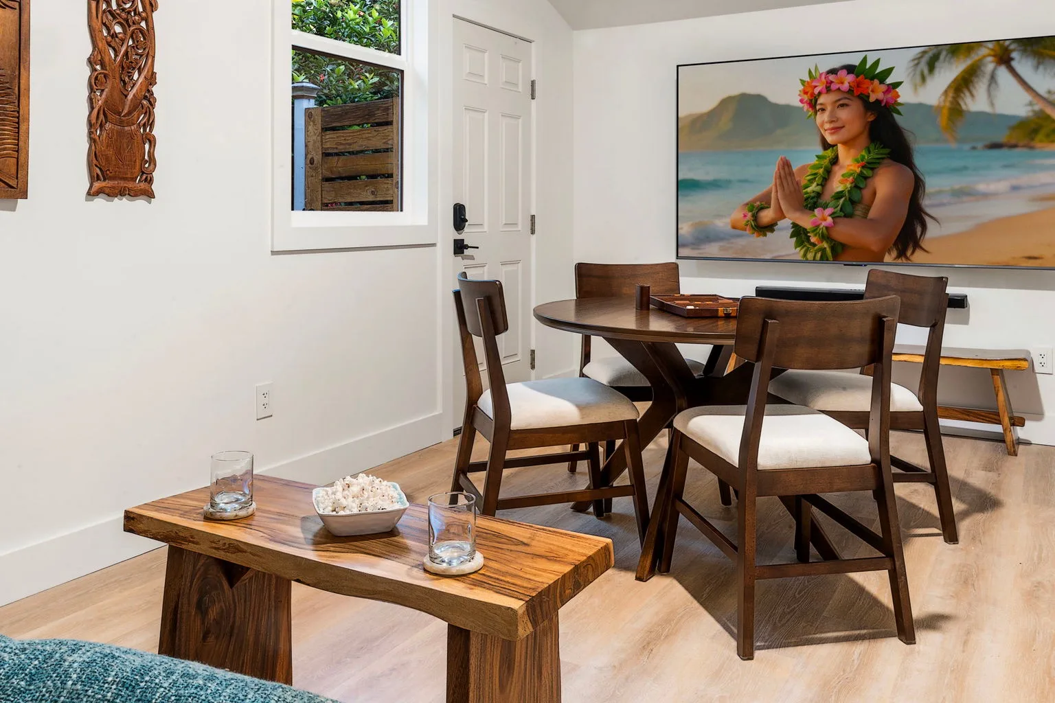 A dining area with a wooden table and chairs beside a large beach-themed wall image.
