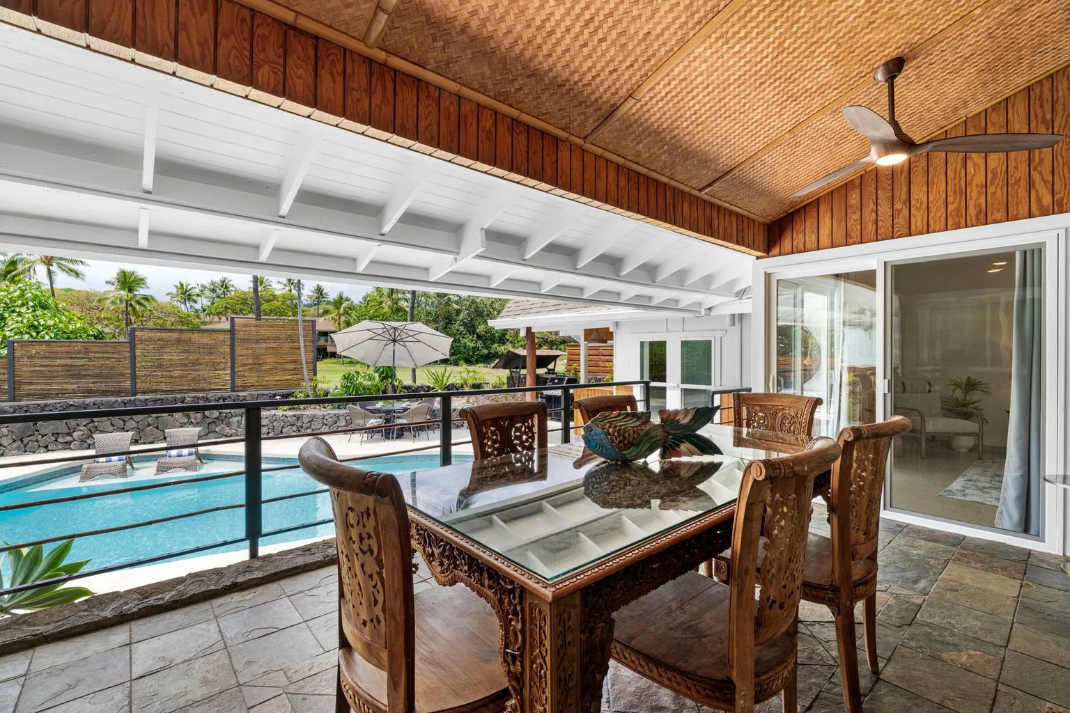 A covered outdoor dining area overlooks a swimming pool and garden.