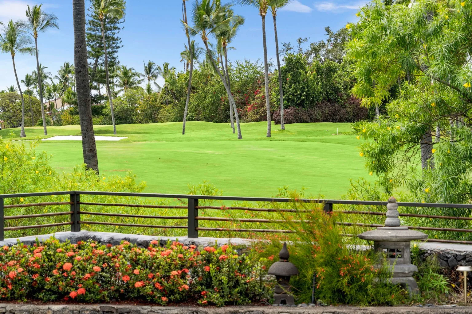 A landscaped garden borders a broad green lawn with palm trees.