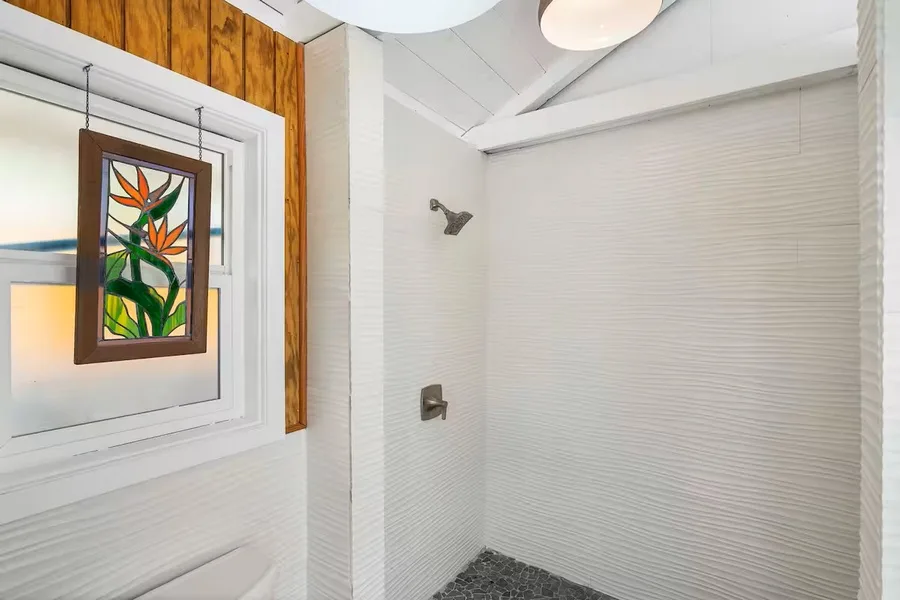 A tiled shower area with a wall-mounted showerhead and colorful framed artwork nearby.
