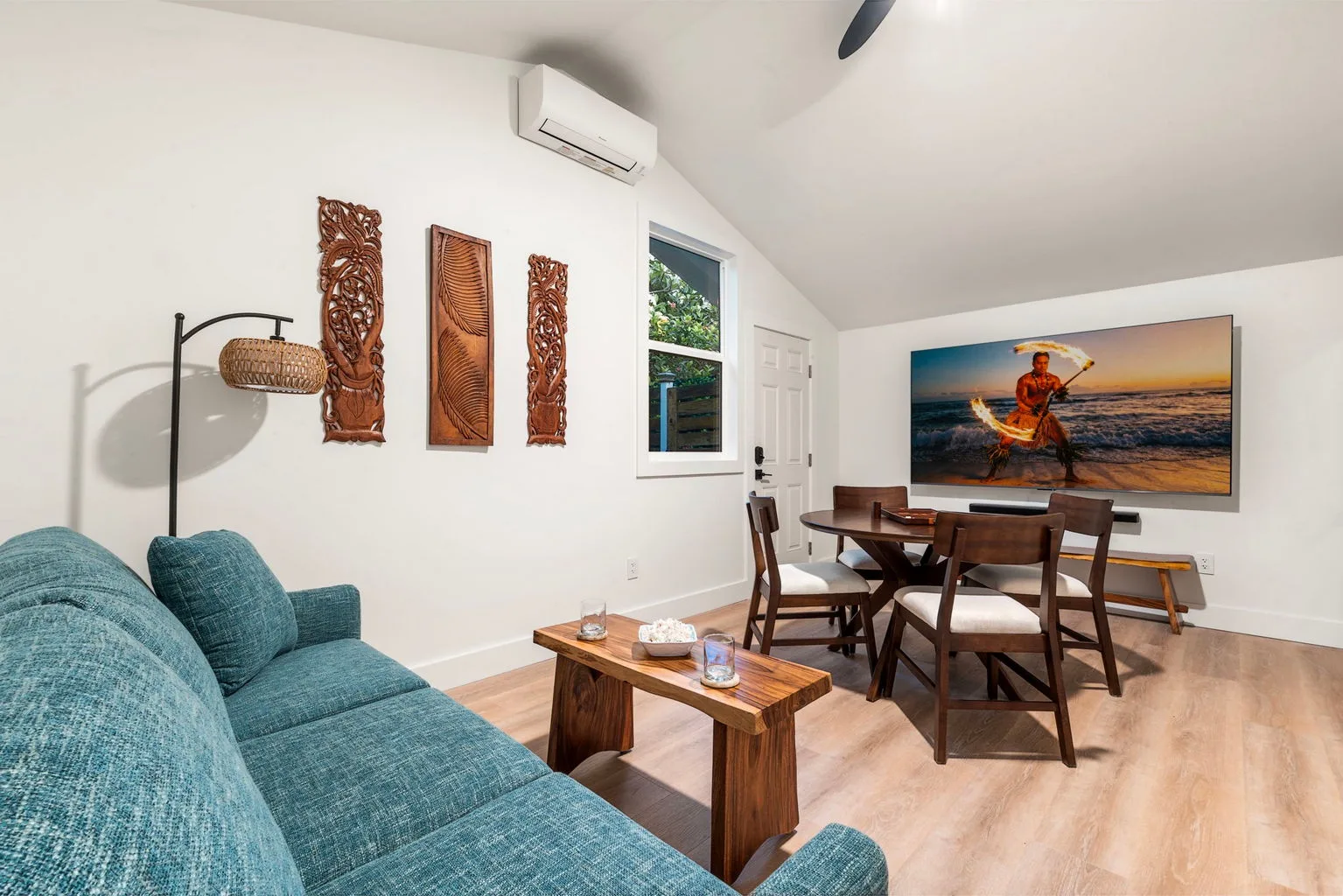 A bright living and dining area with teal seating and a wooden dining table.