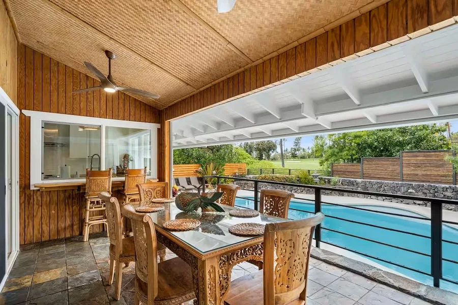 A covered patio with a dining table and chairs overlooks a swimming pool.