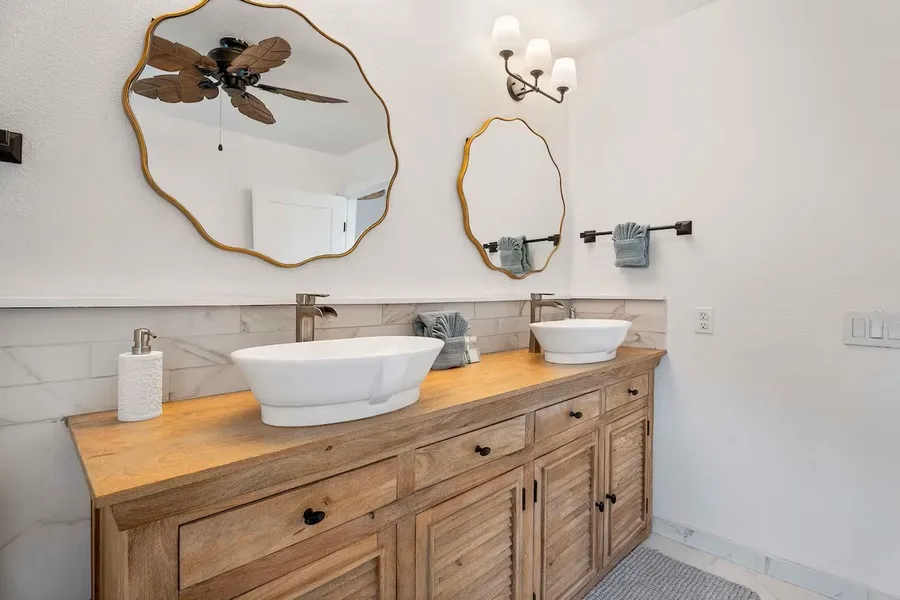 A bathroom vanity with two sinks sits beneath decorative mirrors and wall lights.
