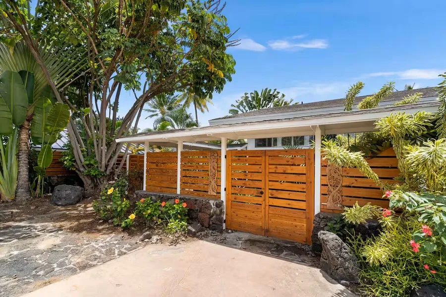 An outdoor entrance with wooden gates, a covered roof, and tropical plants.