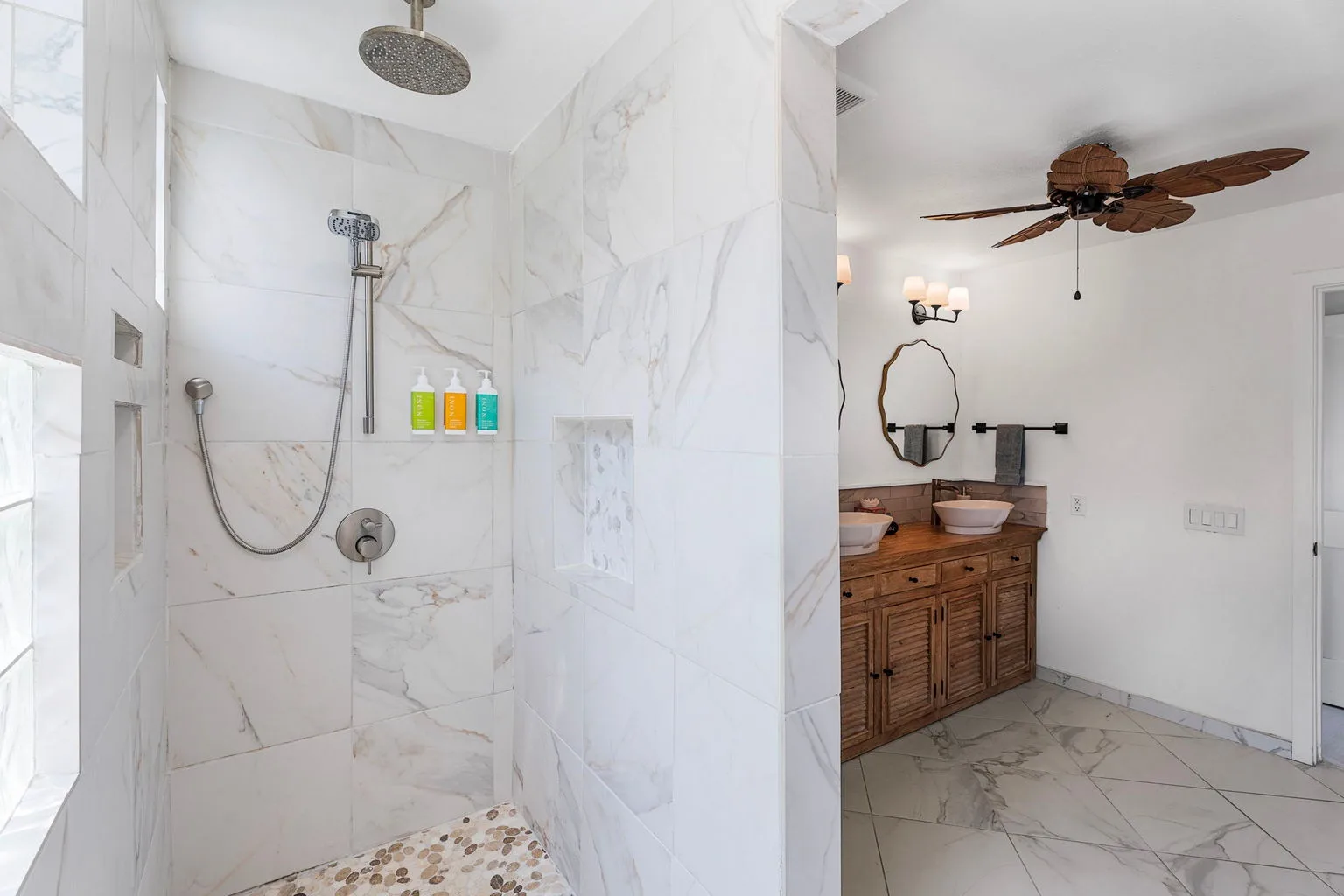A marble-tiled shower opens onto a bathroom vanity with a mirror.