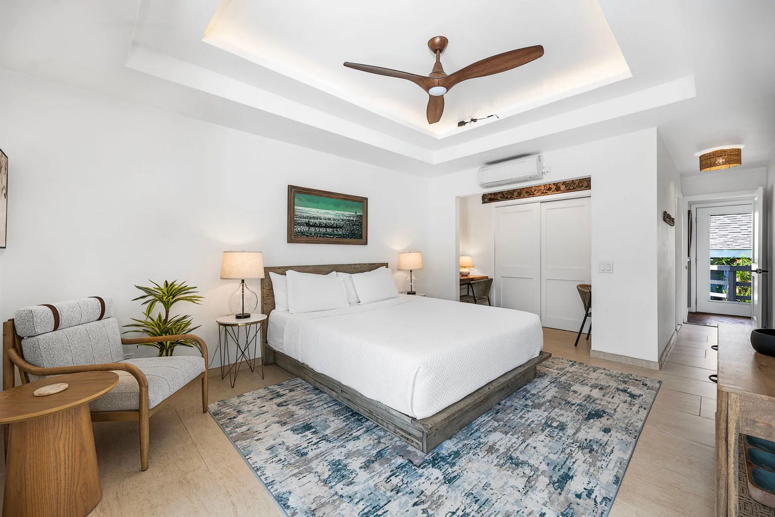 A bright bedroom with a bed, seating, and a ceiling fan.