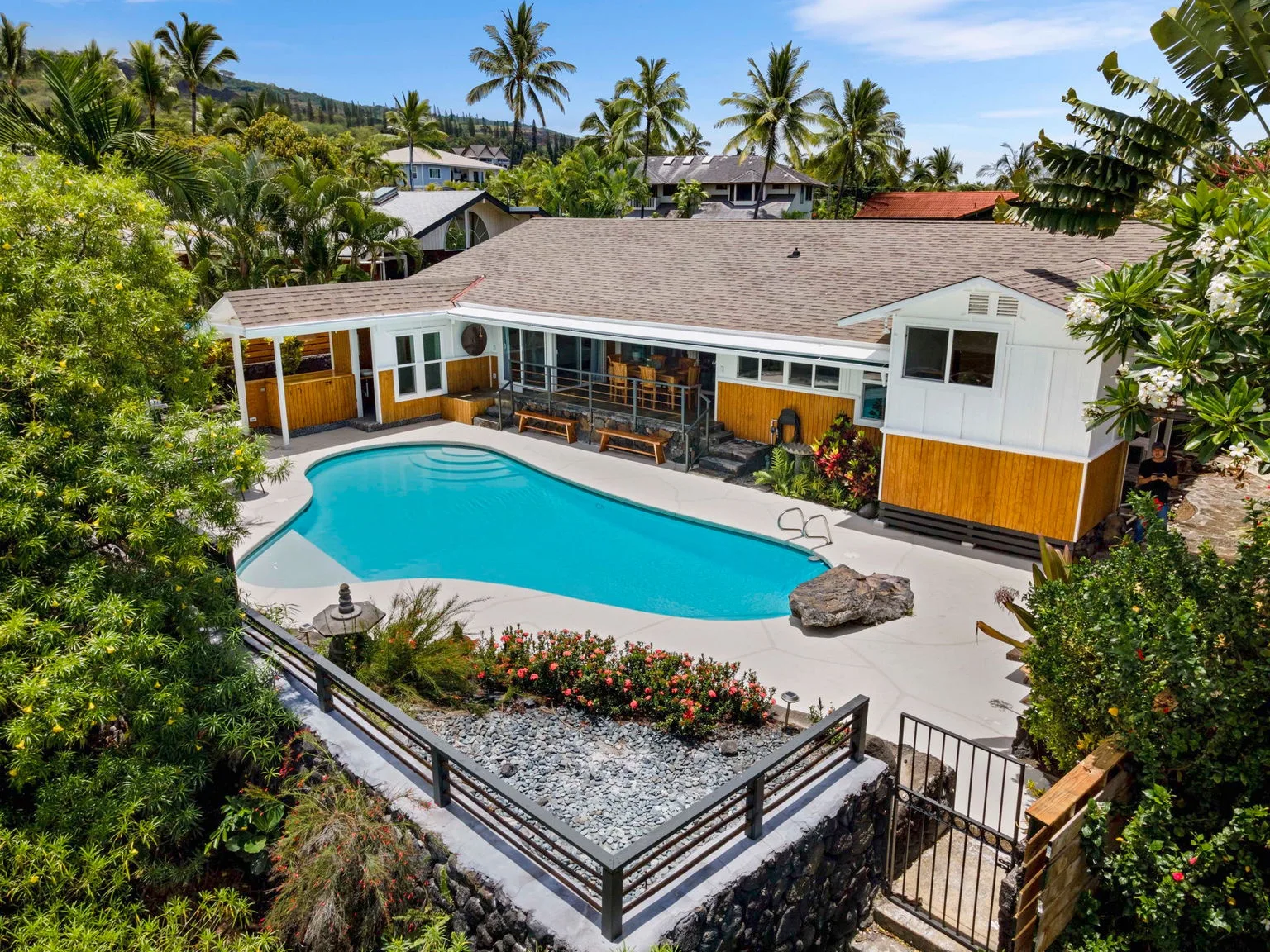 A tropical house with a turquoise swimming pool and lush greenery.