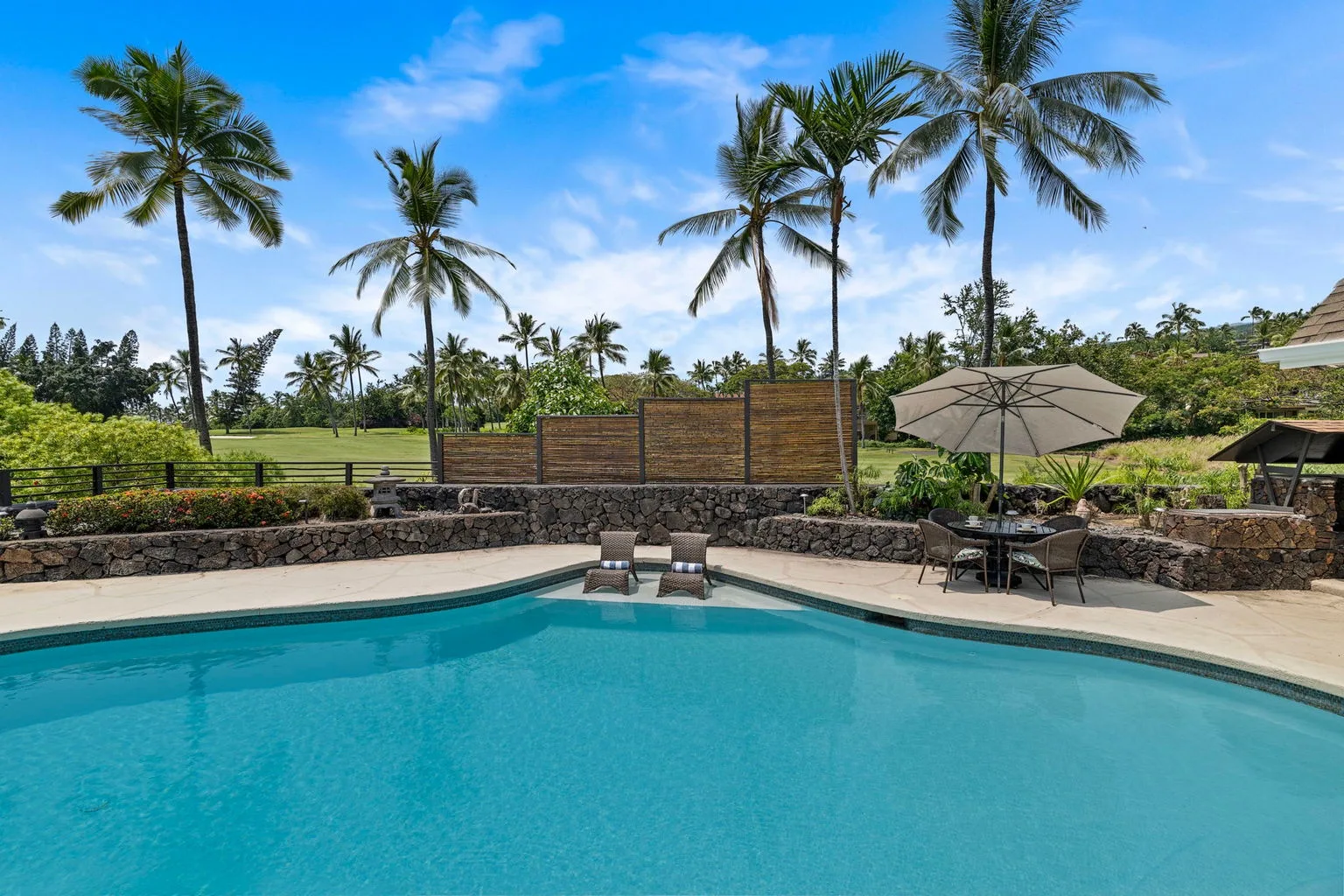 A turquoise swimming pool sits beside palm trees and shaded outdoor seating.