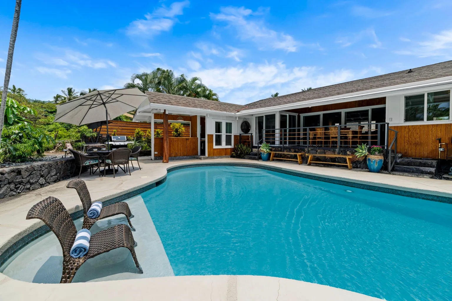 A swimming pool sits beside a patio with outdoor seating and a shaded dining area.