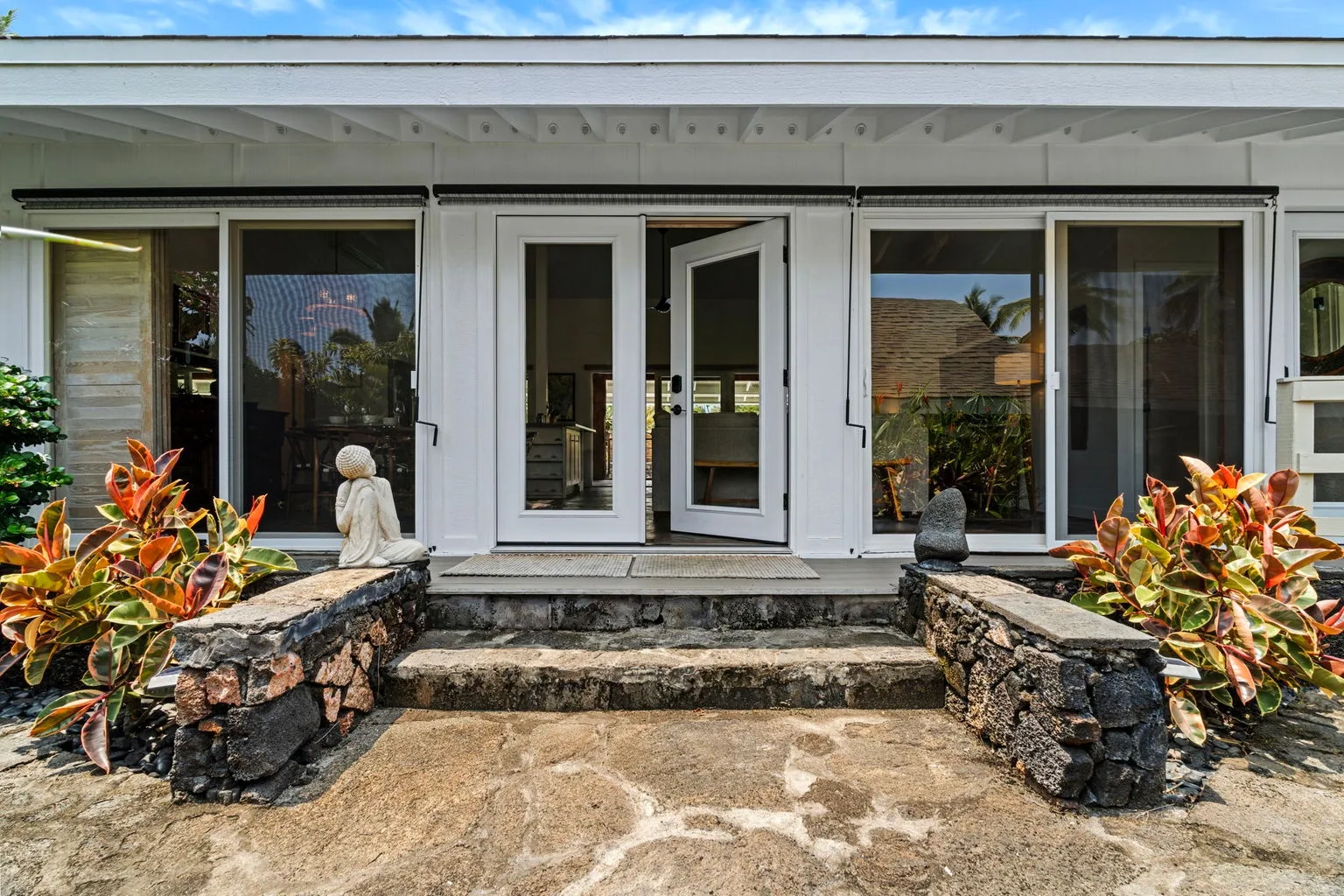 A house entrance with an open glass door and stone steps, framed by plants.