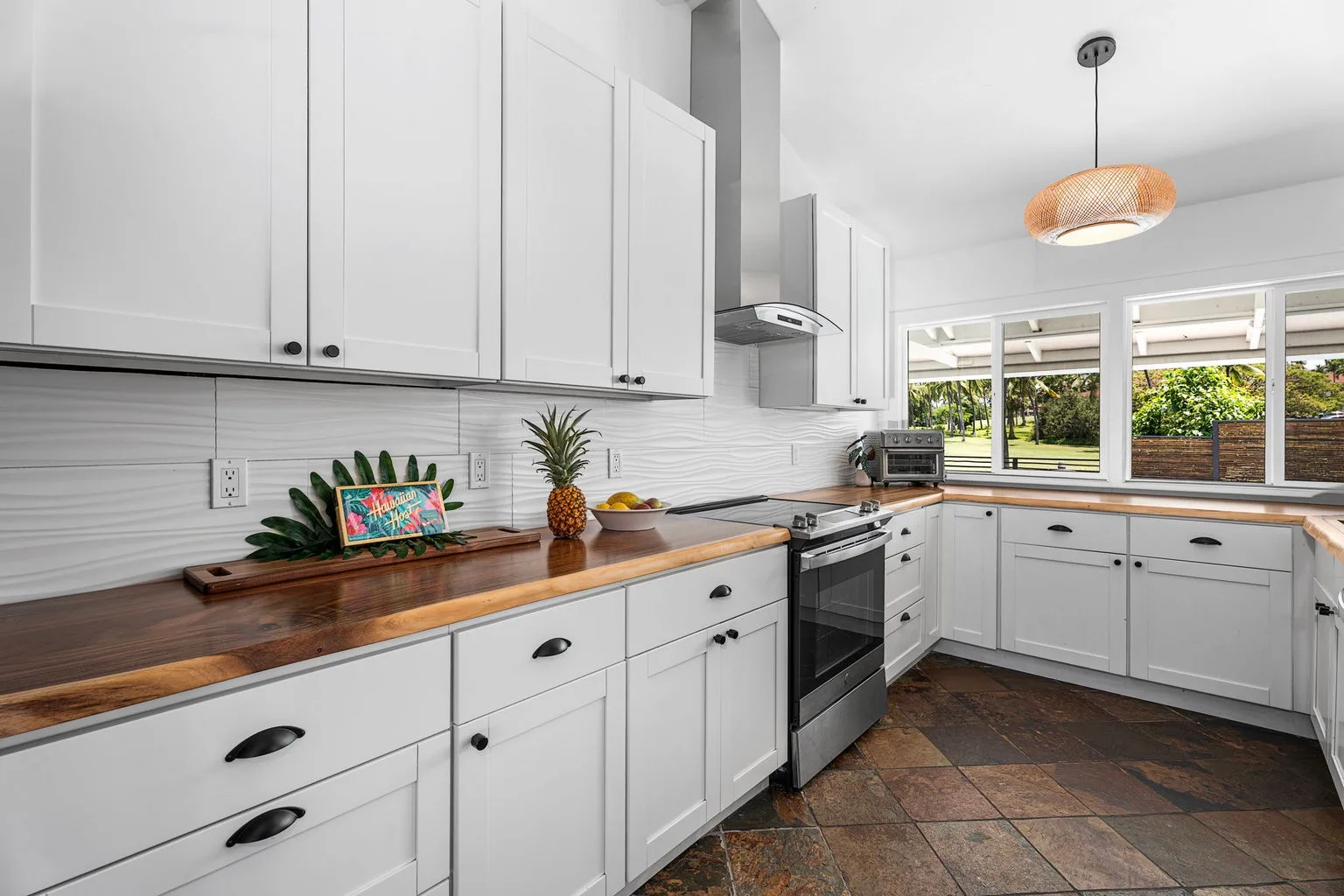 A bright kitchen with white cabinets, wood countertops, and windows overlooking greenery.
