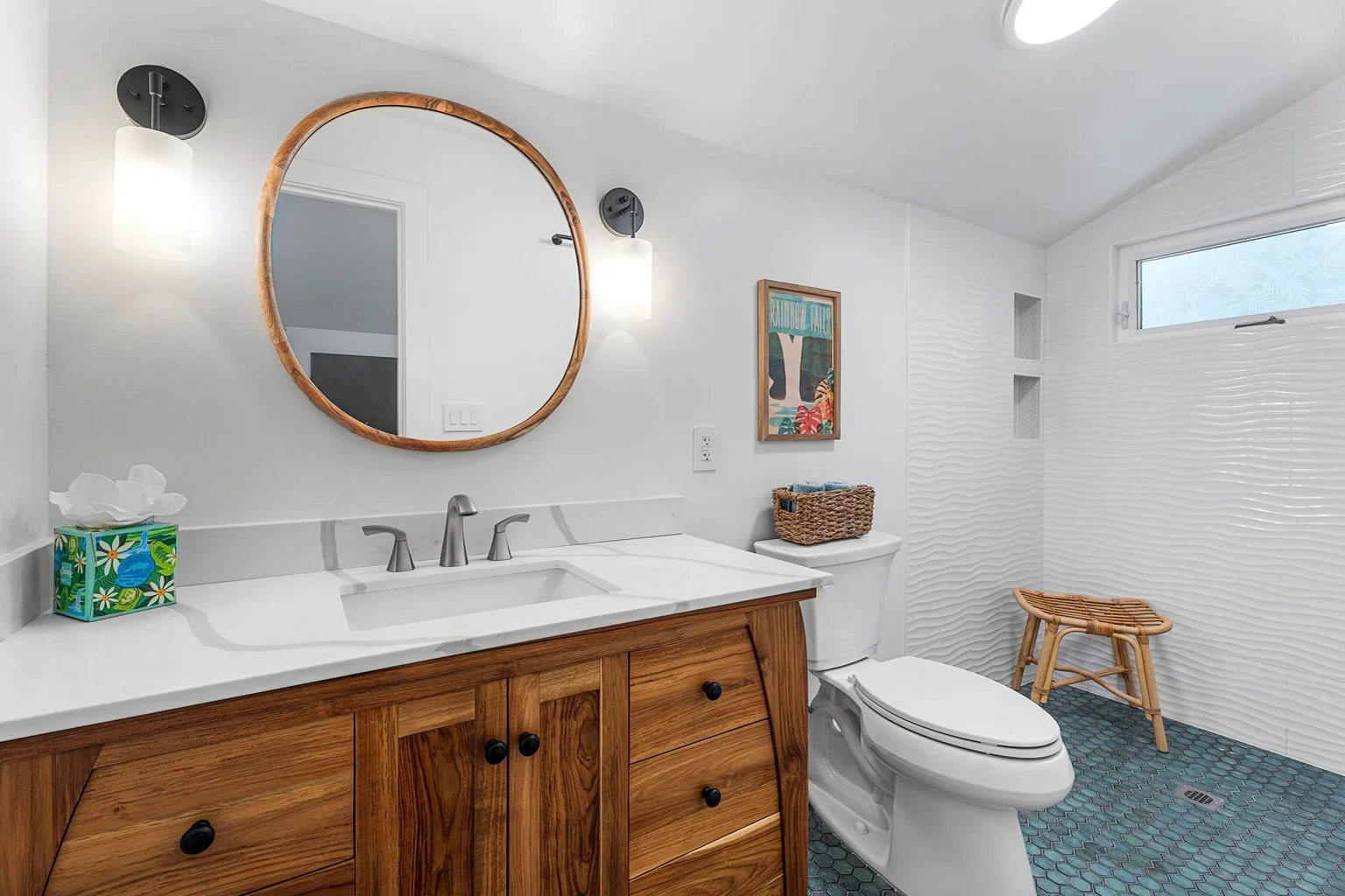 A bright bathroom with a long vanity, round mirror, and toilet.