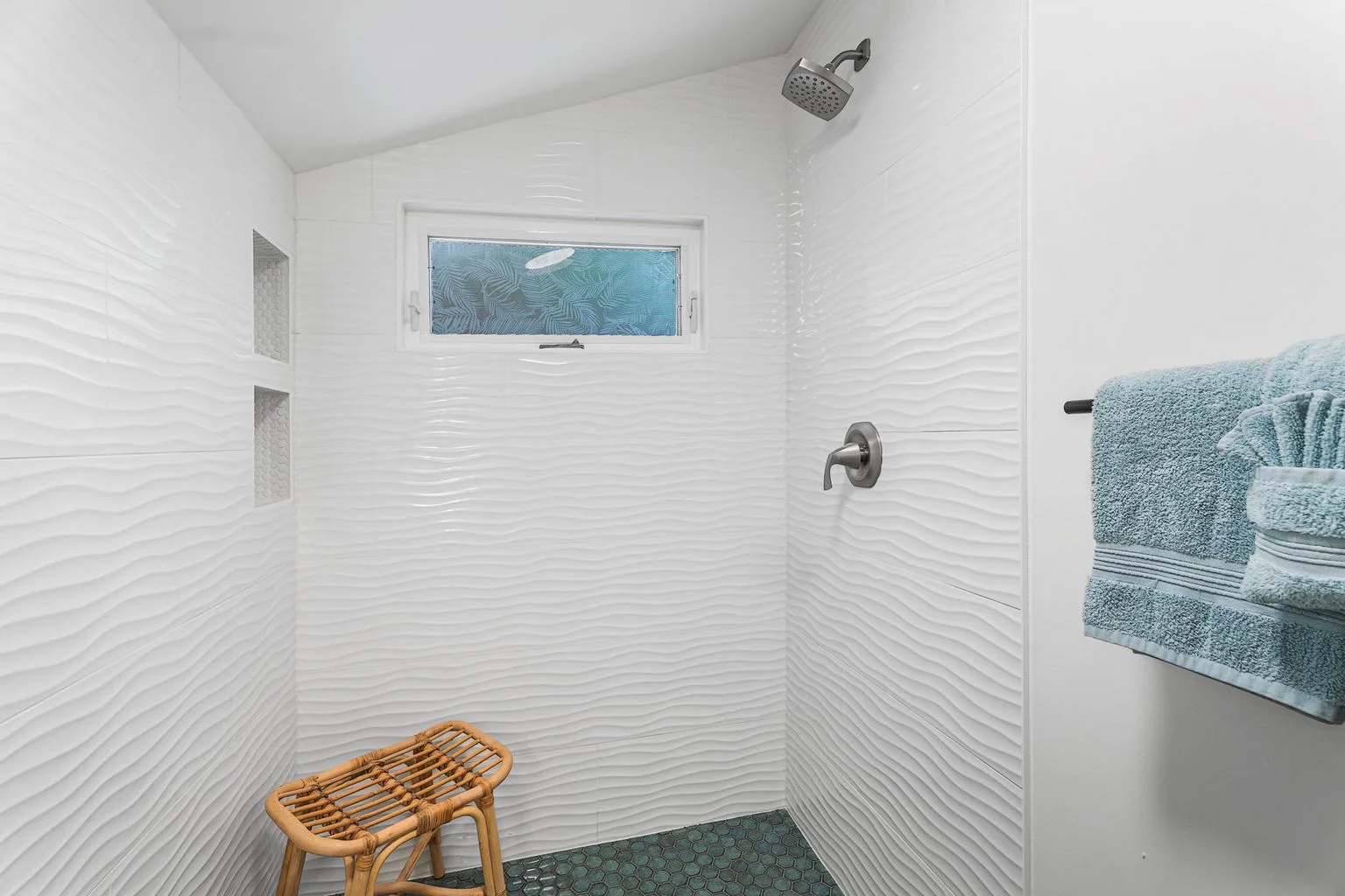 A tiled shower area with a small window and a wooden stool.