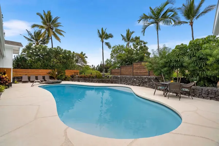 An outdoor swimming pool is surrounded by a pale patio and palm trees.