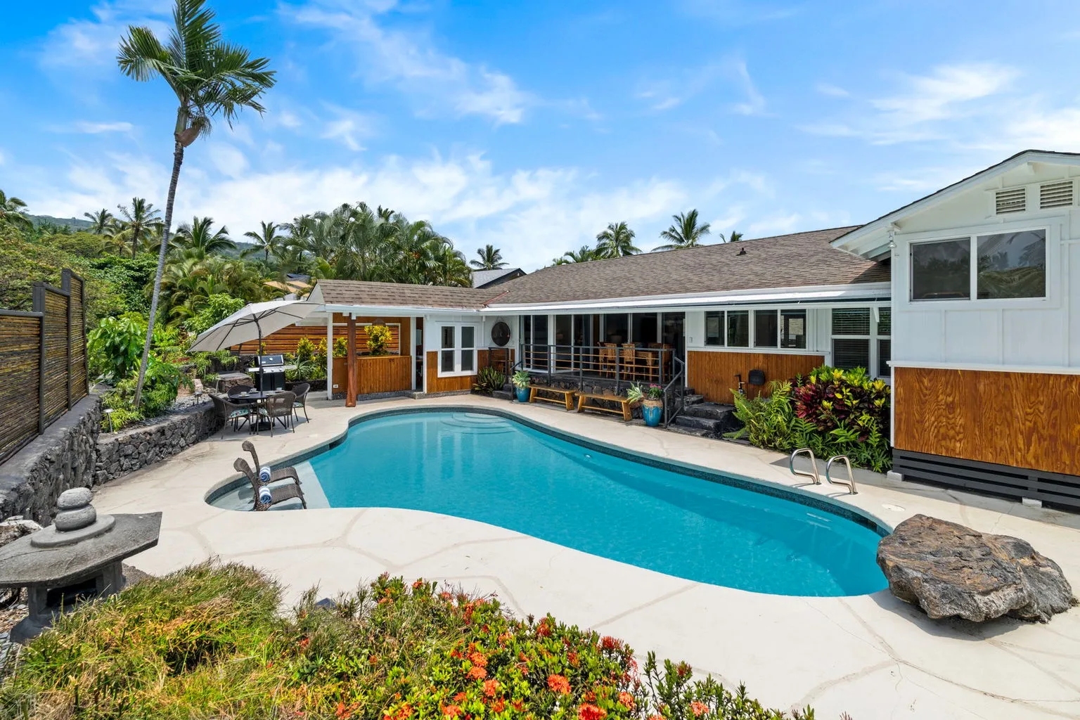 An outdoor swimming pool sits beside a low building and garden.