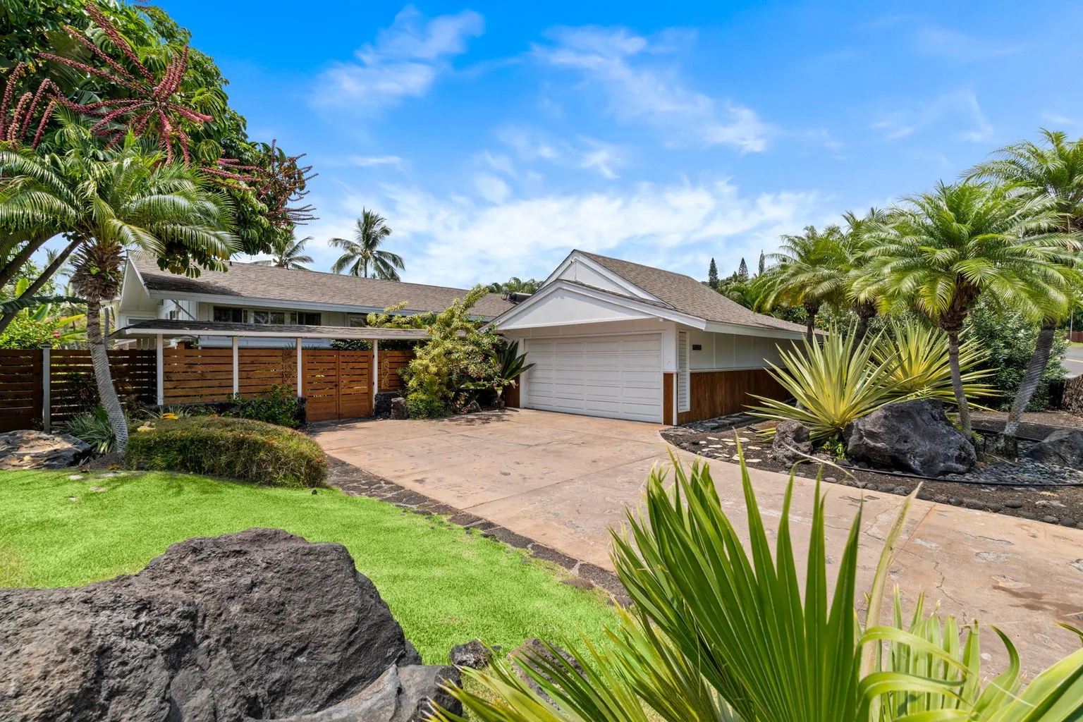 A house with a driveway and garage, surrounded by palm trees and landscaping.