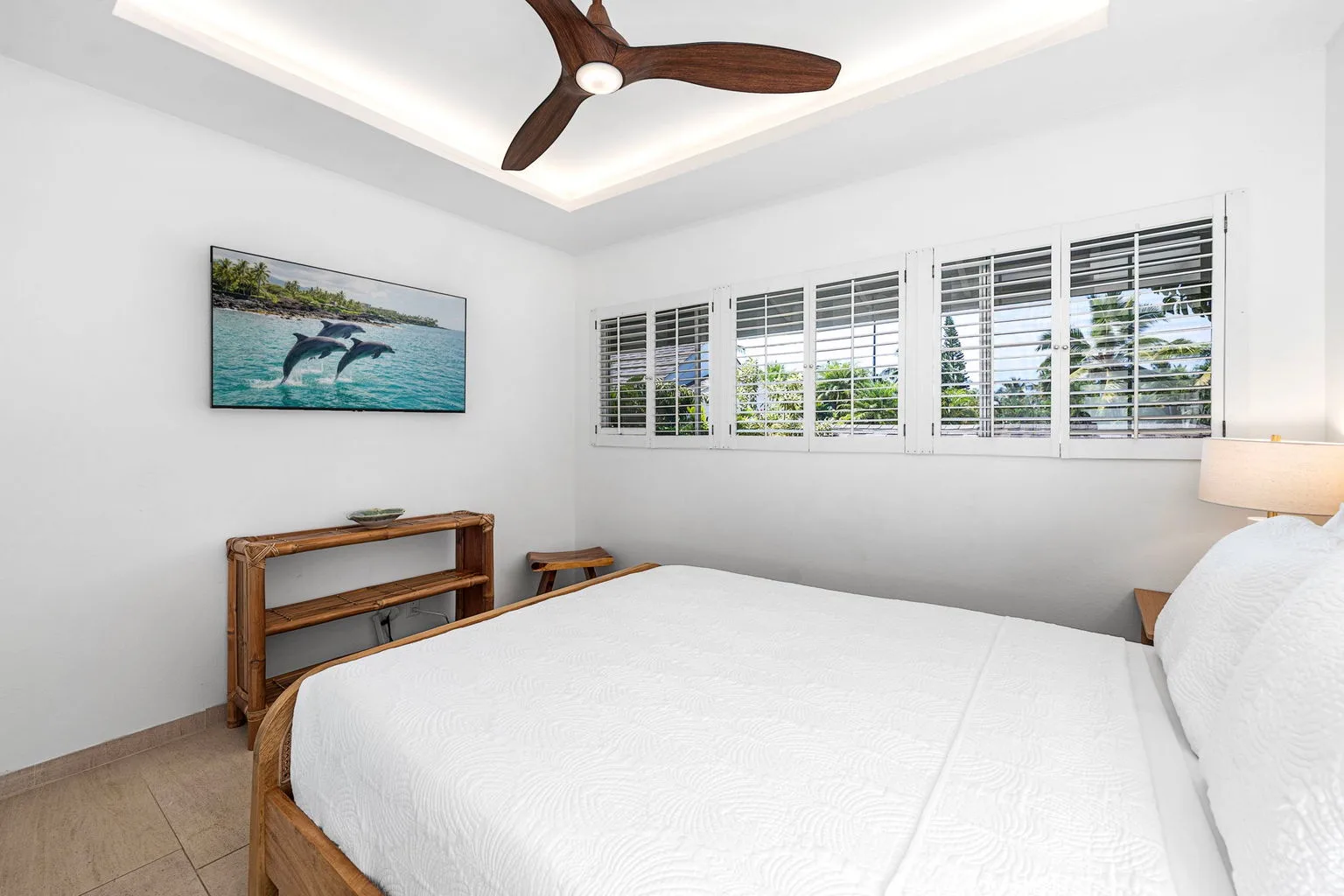 A bright bedroom with a white bed, shuttered windows, and a ceiling fan.