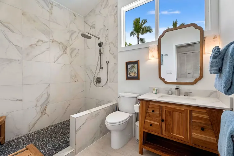 A bright bathroom with a shower, toilet, and wooden vanity beneath a framed mirror.