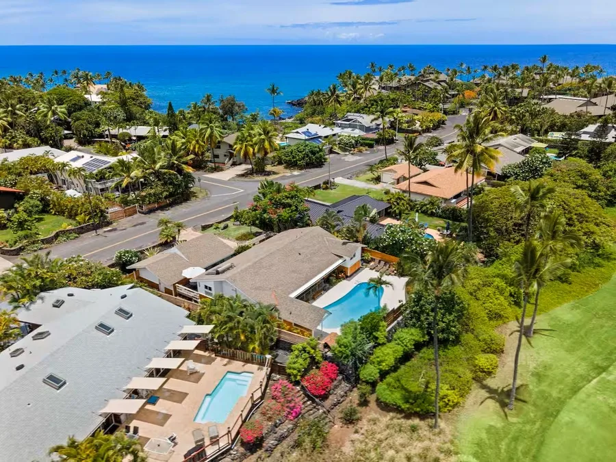 Aerial view of tropical homes, pools, and palm trees beside the ocean.