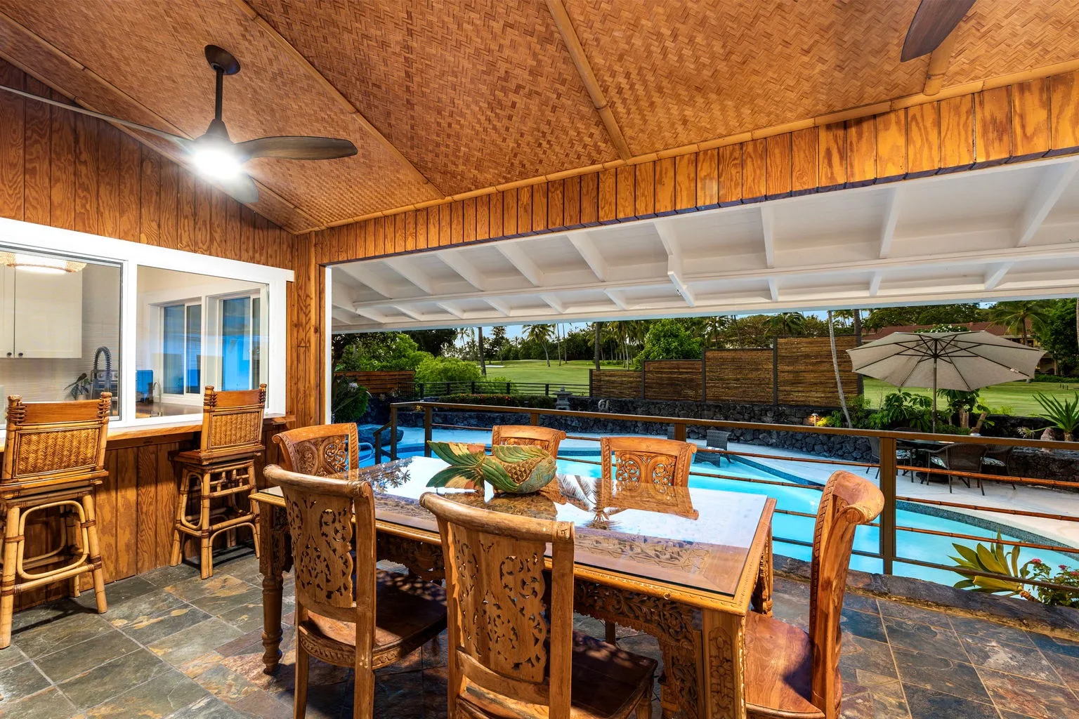 A wooden dining table and seating sit beside a covered swimming pool.