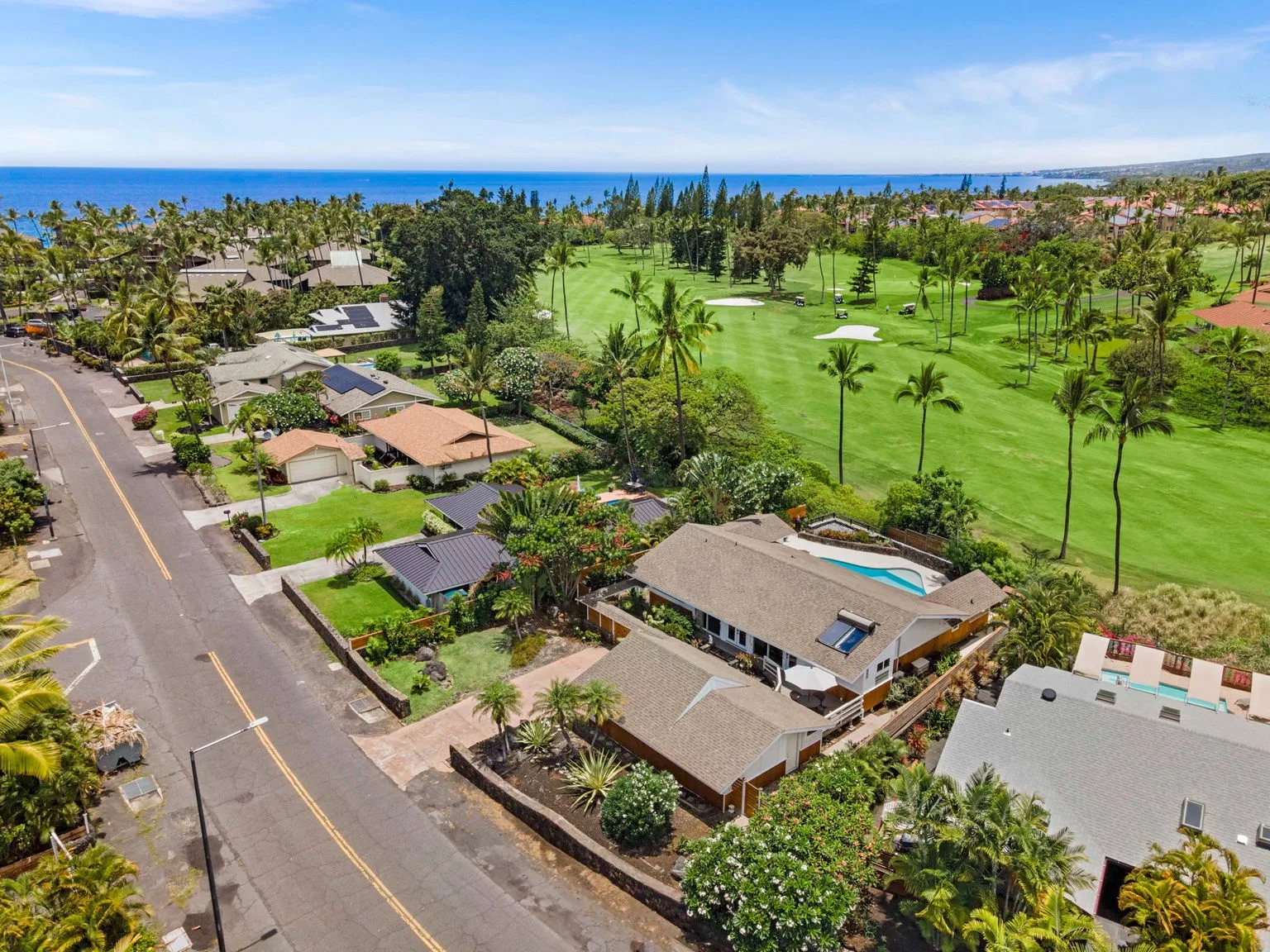 Aerial view of a coastal golf course bordered by homes and palm trees.