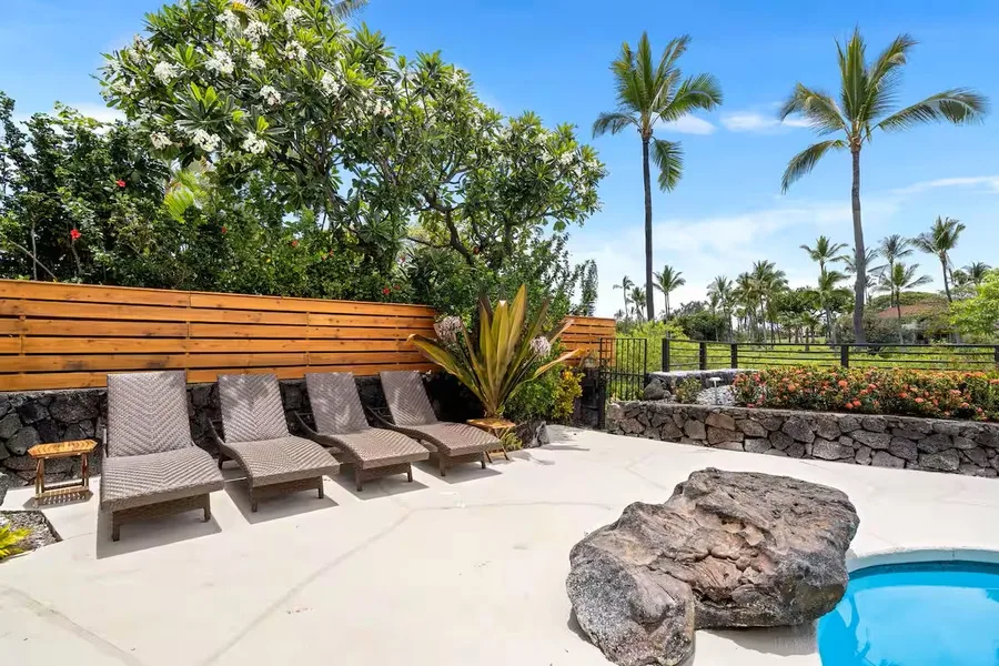 A sunny poolside patio with lounge seating and tropical plants.