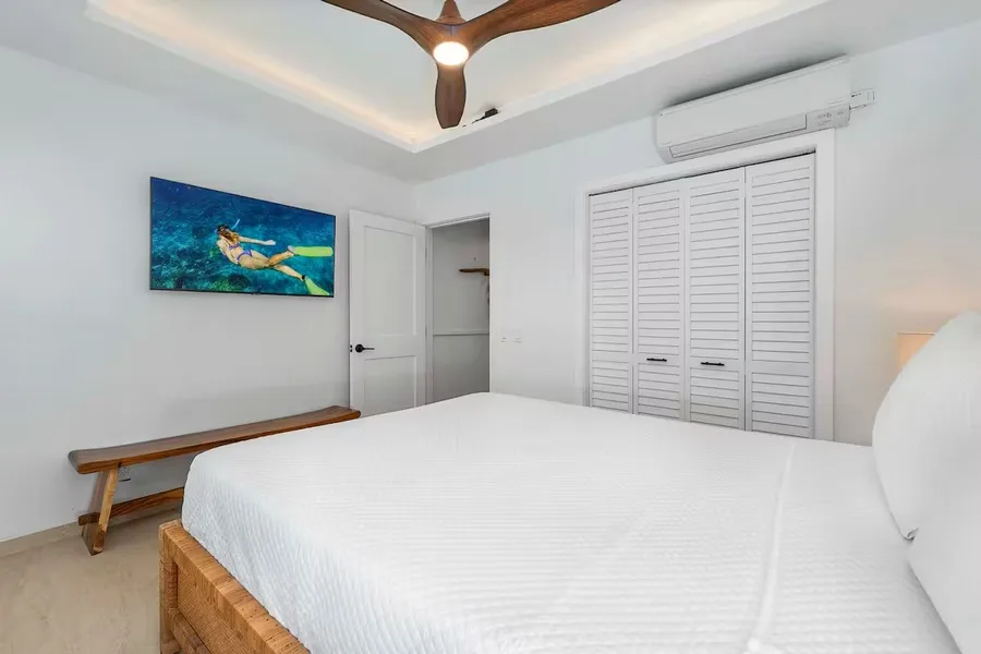 A bedroom with a white bed, a wall-mounted television, and louvered closet doors.
