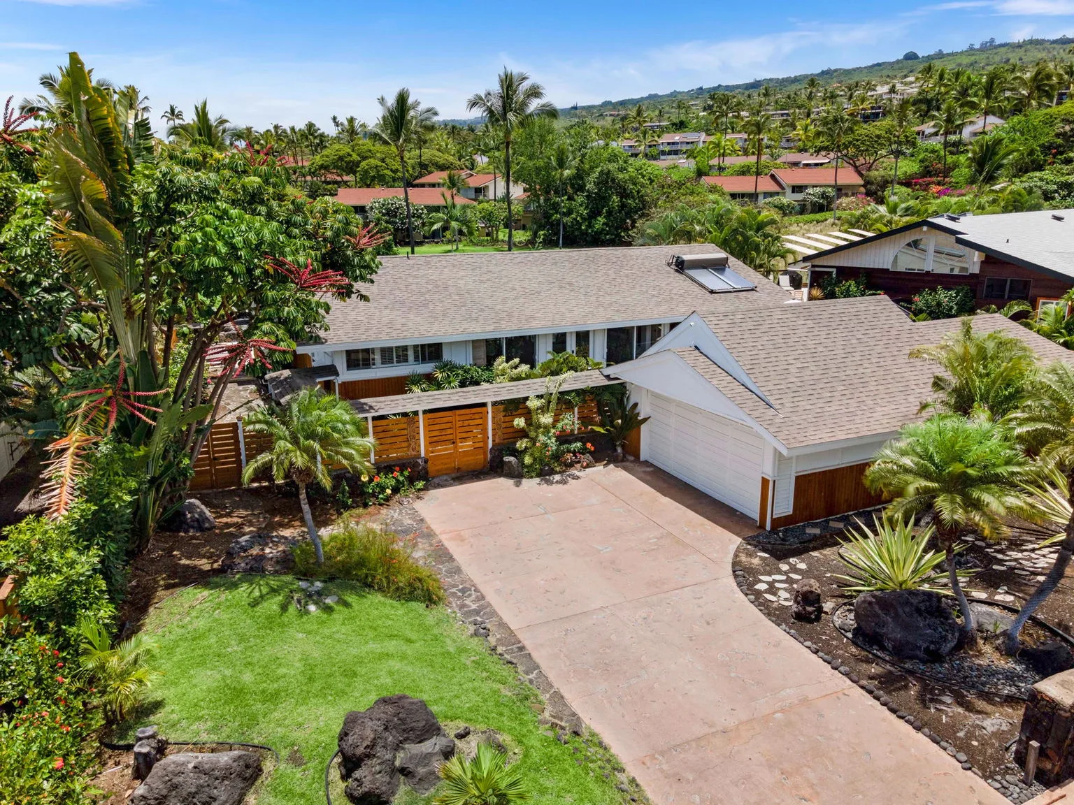 Aerial view of a single-story home with a driveway and lush landscaping.