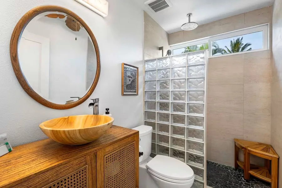 A bathroom with a wooden vanity, vessel sink, toilet, and glass-block shower wall.