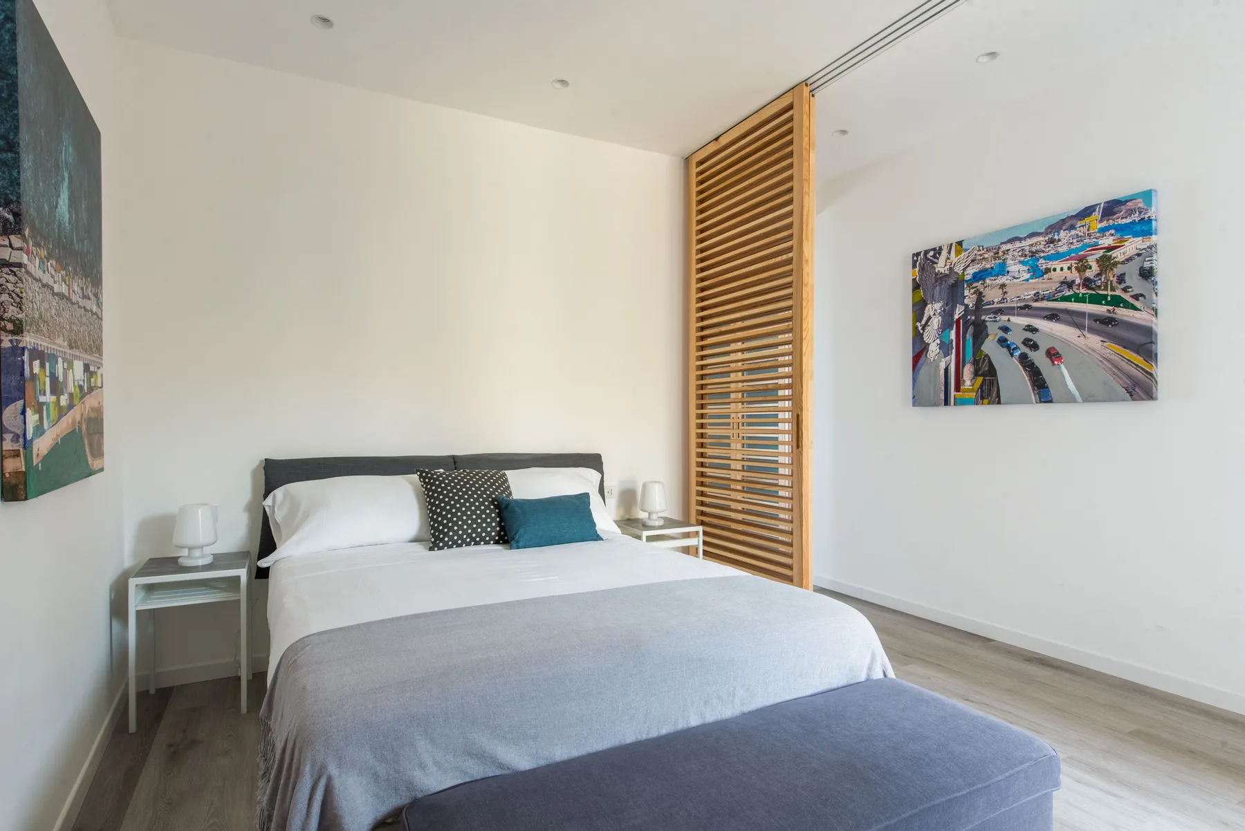 A bright bedroom with a neatly made bed and colorful wall art.