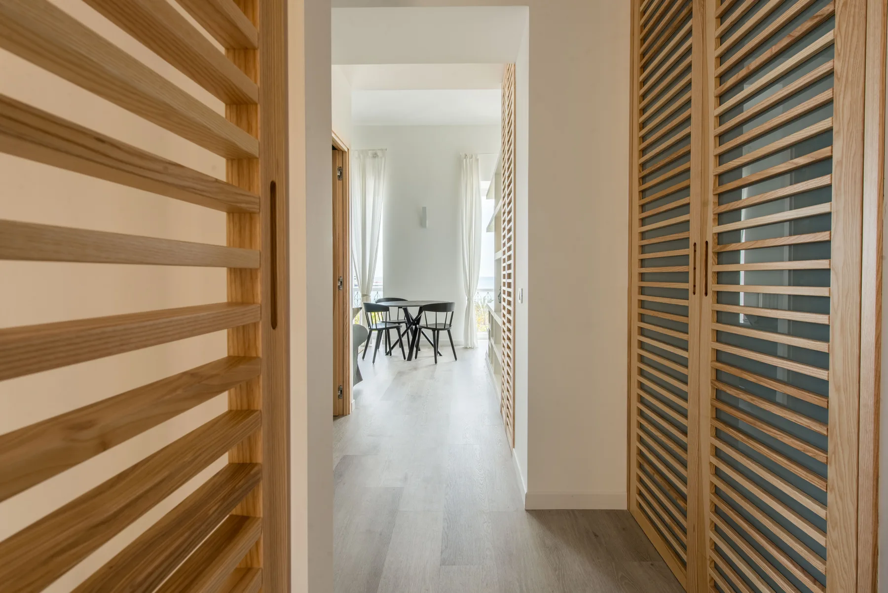 A hallway with wooden slatted doors opens onto a bright dining area.