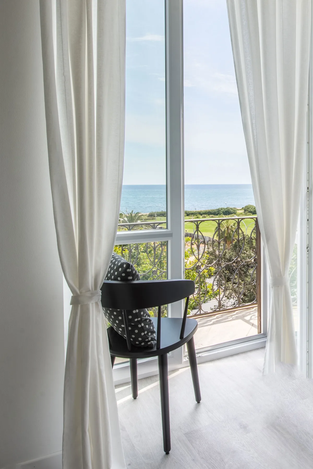 A chair sits beside an open glass door overlooking the sea.