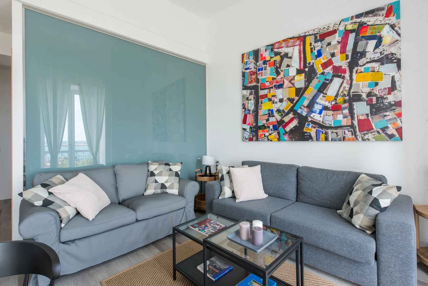 A living room with gray seating, a glass coffee table, and colorful wall art.