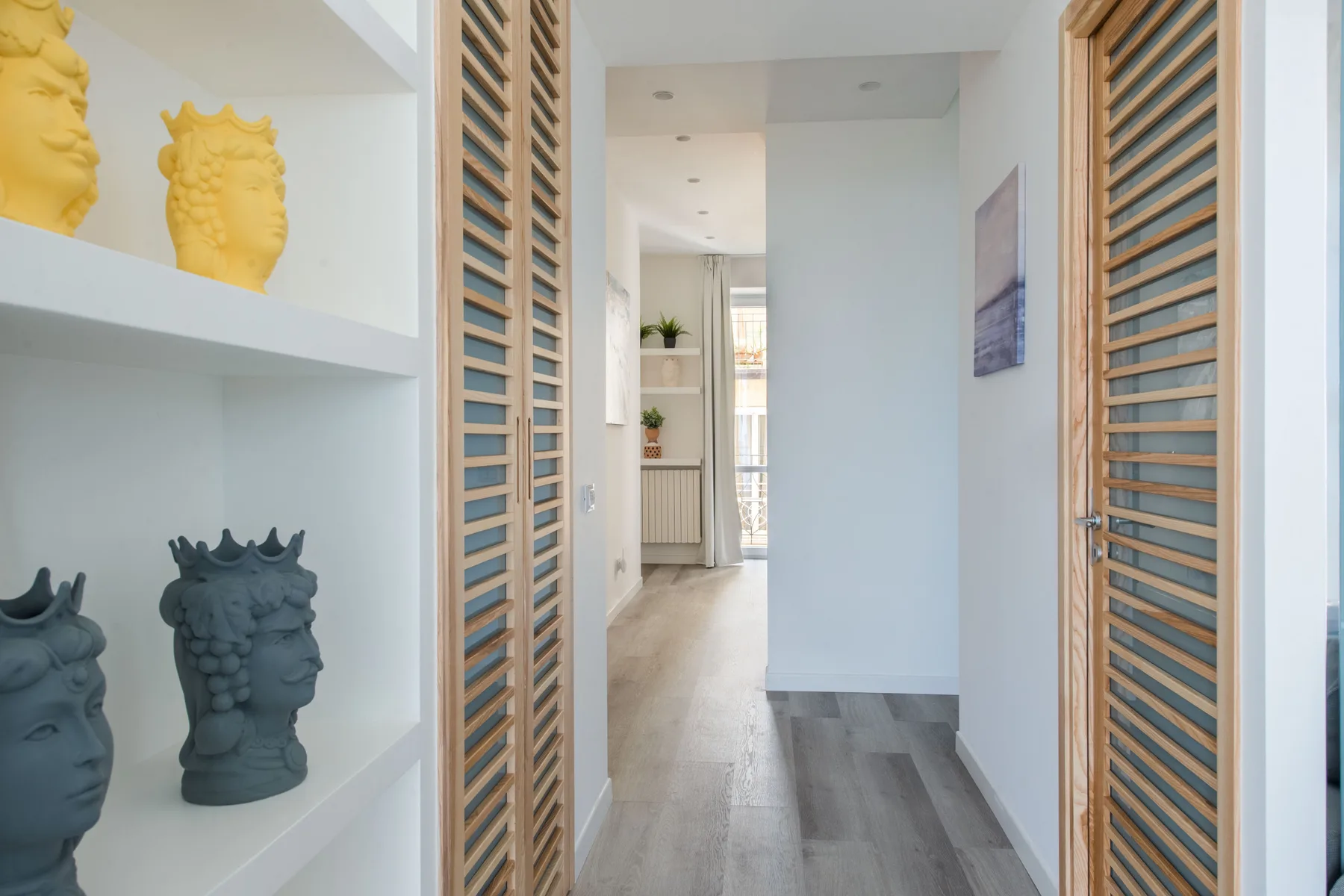 A bright hallway with wooden louvered doors and decorative sculptures on built-in shelves.