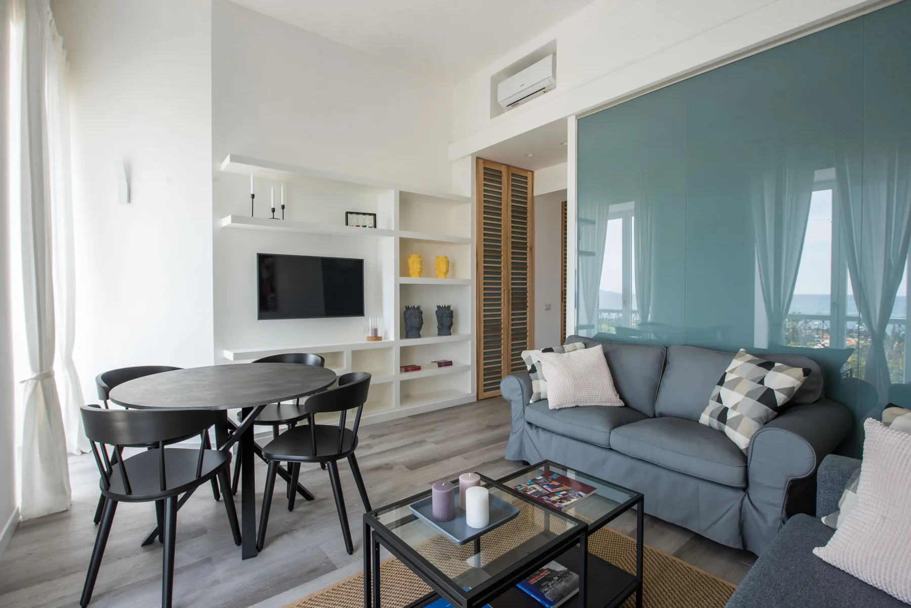 A bright living room with a gray sofa, dining table, and television.