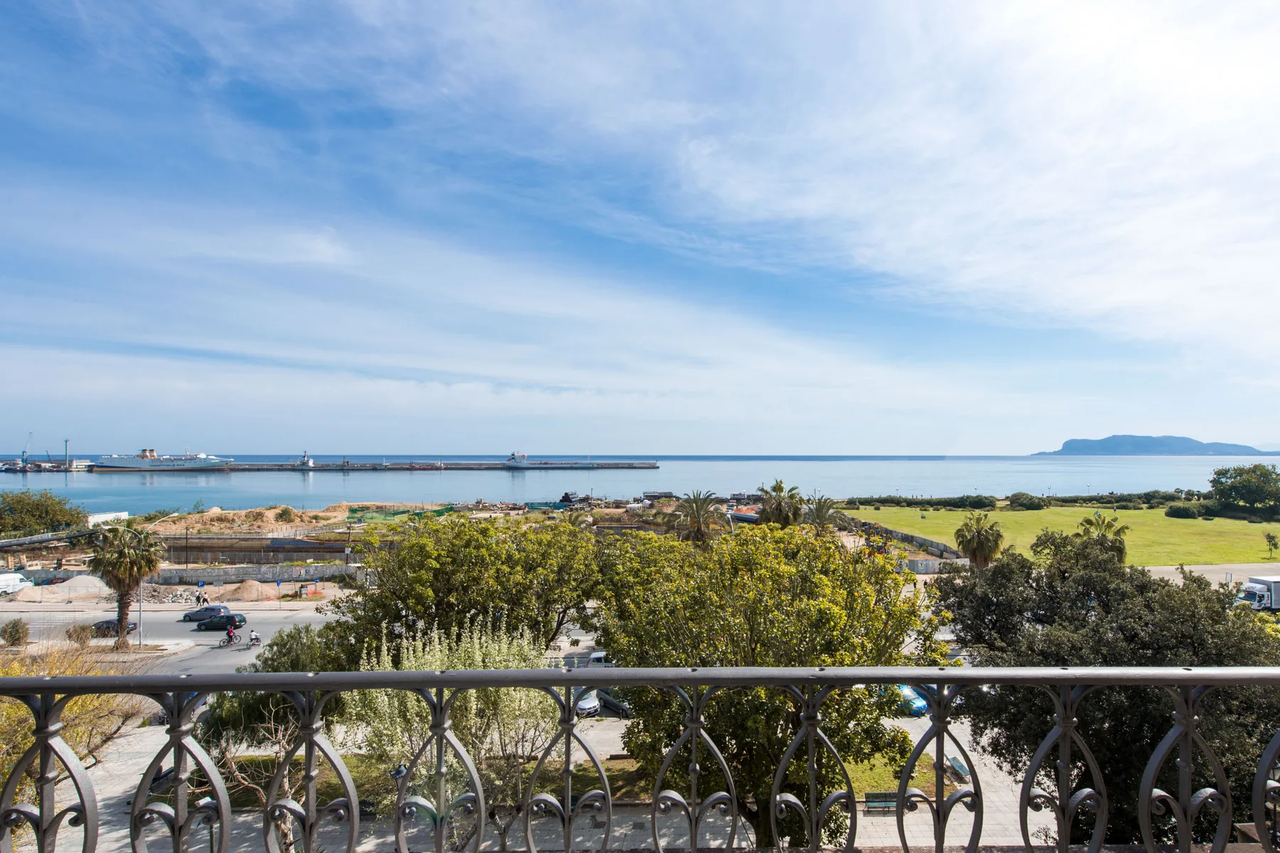 A balcony overlooks landscaped grounds, the coastline, and a calm blue sea.