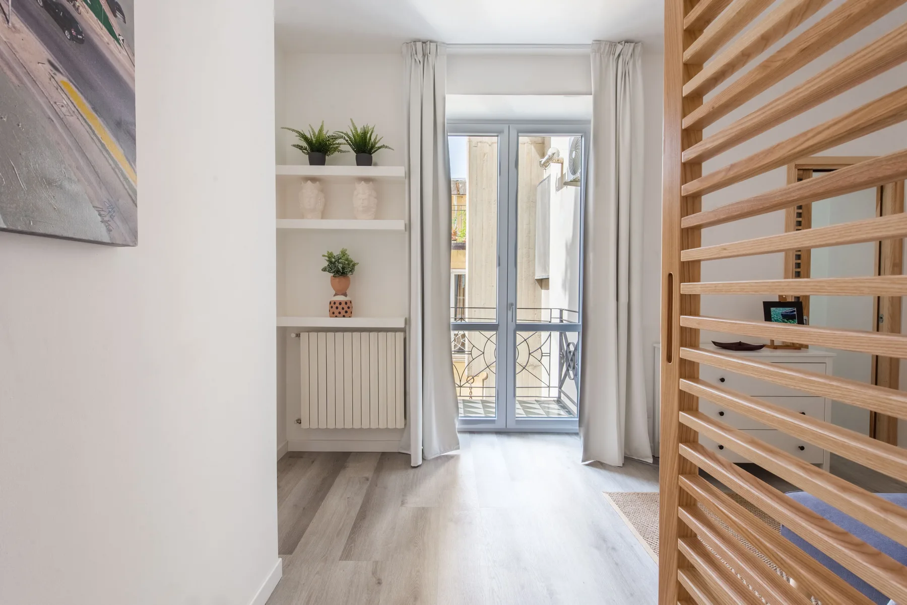 A bright interior hallway opens onto a glass balcony door, with shelving along the wall.