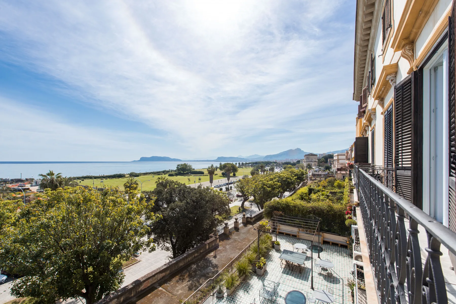 A balcony overlooks a seaside landscape with trees and distant hills.