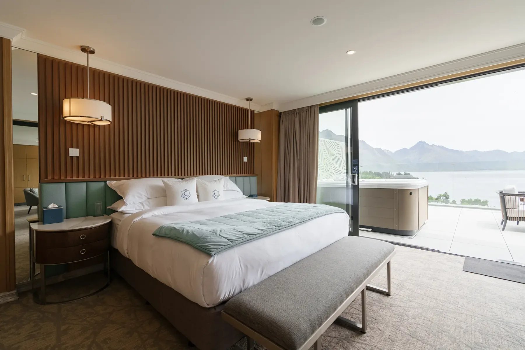 Modern hotel bedroom opening onto a balcony with a spa pool and mountain-lake view.