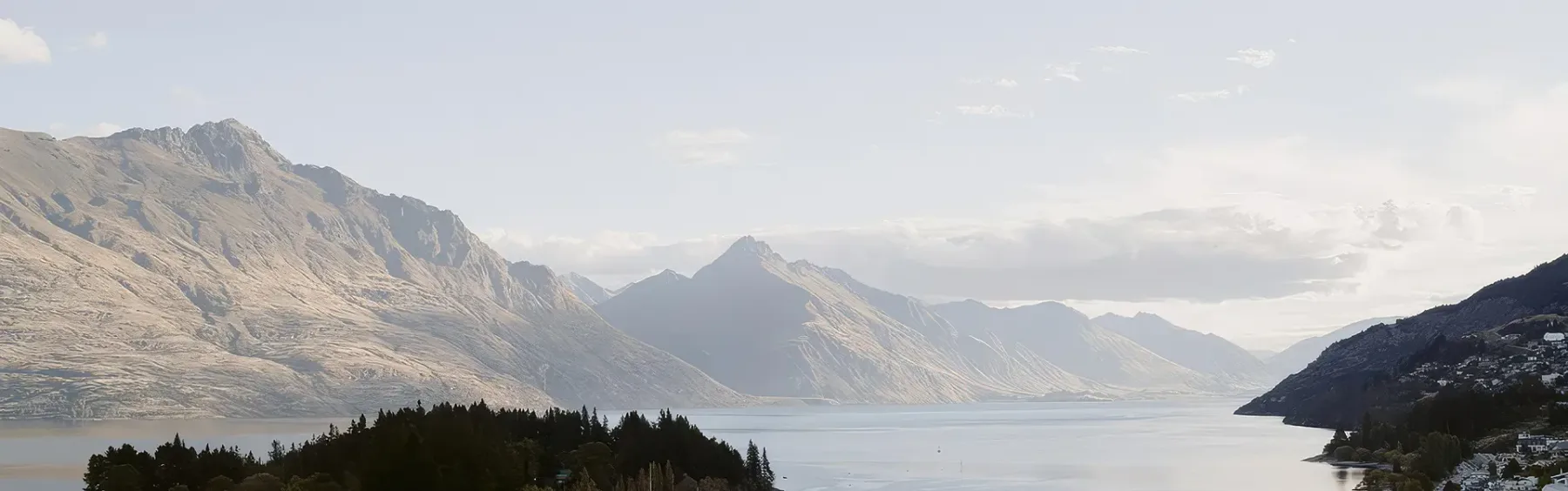 Wide lake surrounded by rugged mountains under a pale, cloudy sky.