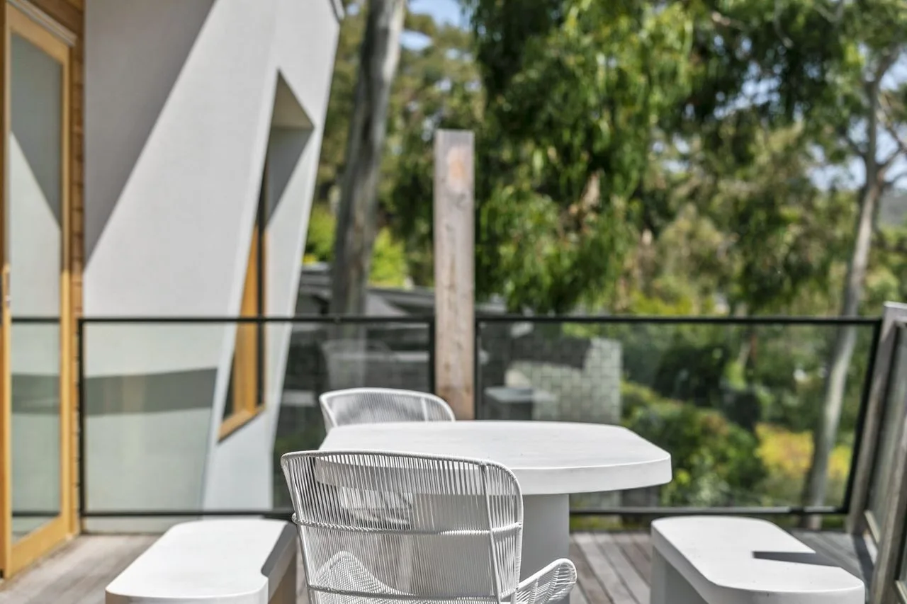 Una zona de estar al aire libre con mesa y sillas junto a una barandilla de vidrio.