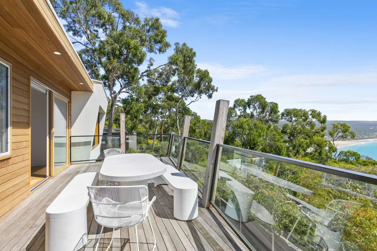 Una terraza de madera con asientos al aire libre da a árboles y colinas lejanas.