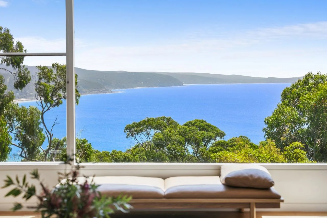 A cushioned outdoor seating area overlooks blue water and a green coastline.