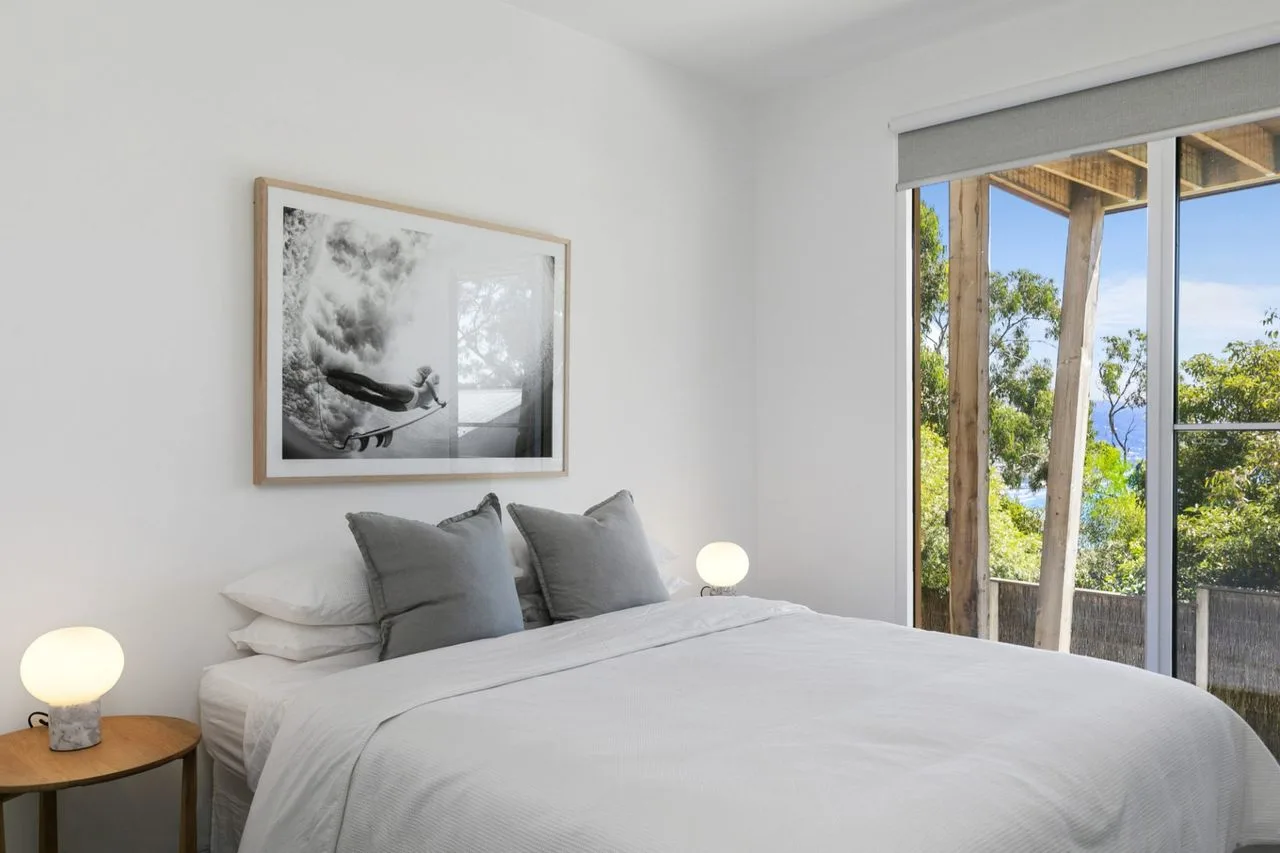 Un dormitorio luminoso con una cama tendida junto a una ventana grande.