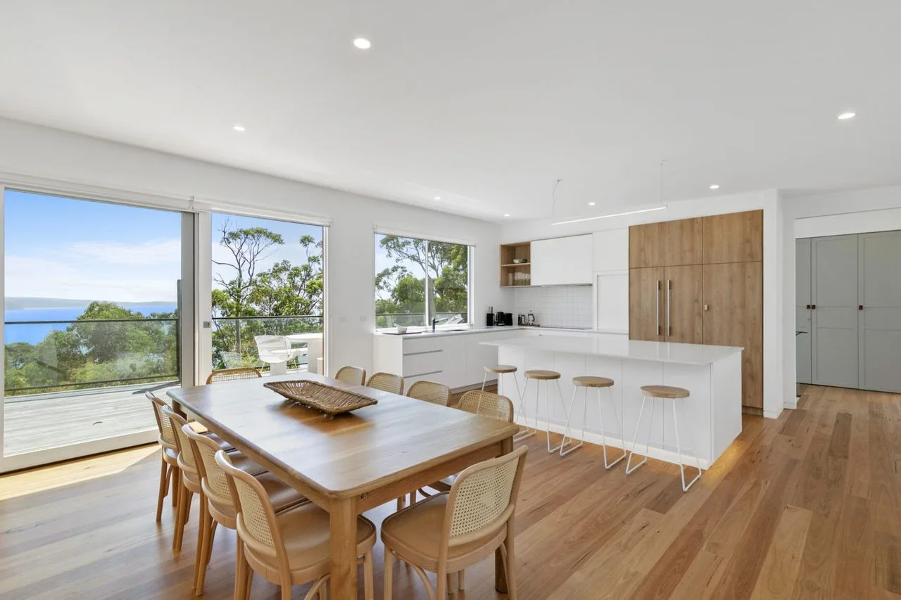 Un comedor luminoso se abre a la cocina, con amplias ventanas con vistas a la vegetación y al agua.