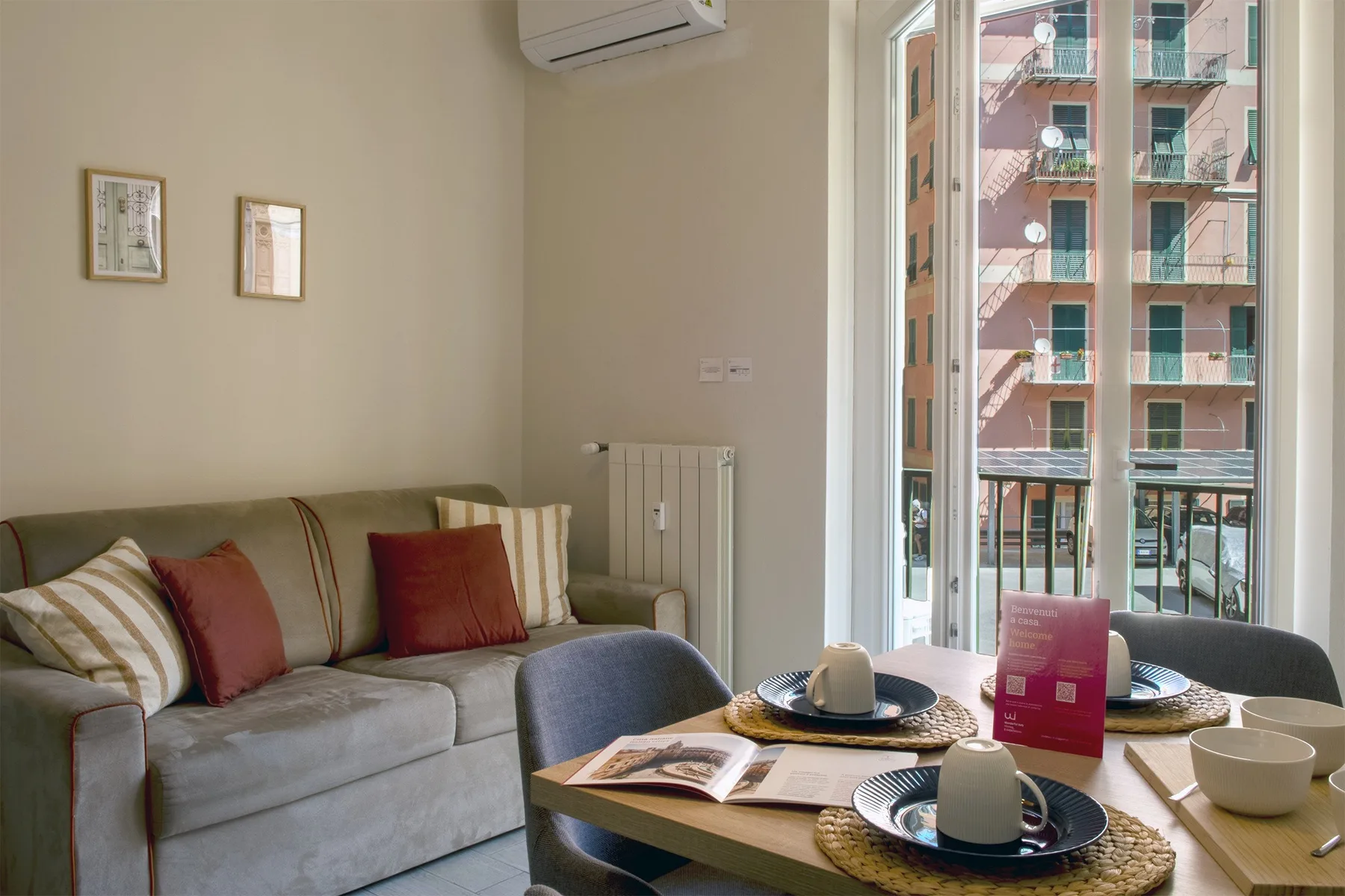 A living room with seating, a dining table, and large windows overlooking nearby buildings.
