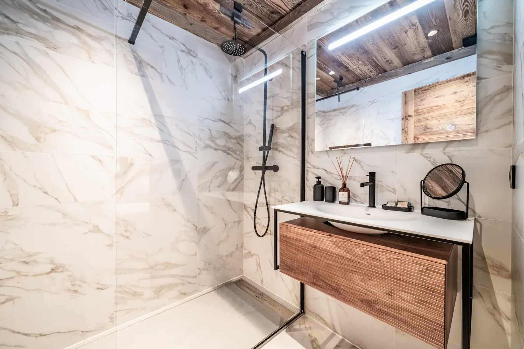 Baño moderno con paredes de mármol, una mampara de ducha de vidrio, un rociador de ducha tipo lluvia, techo de madera, un mueble de baño suspendido con lavabo sobre encimera y accesorios minimalistas.