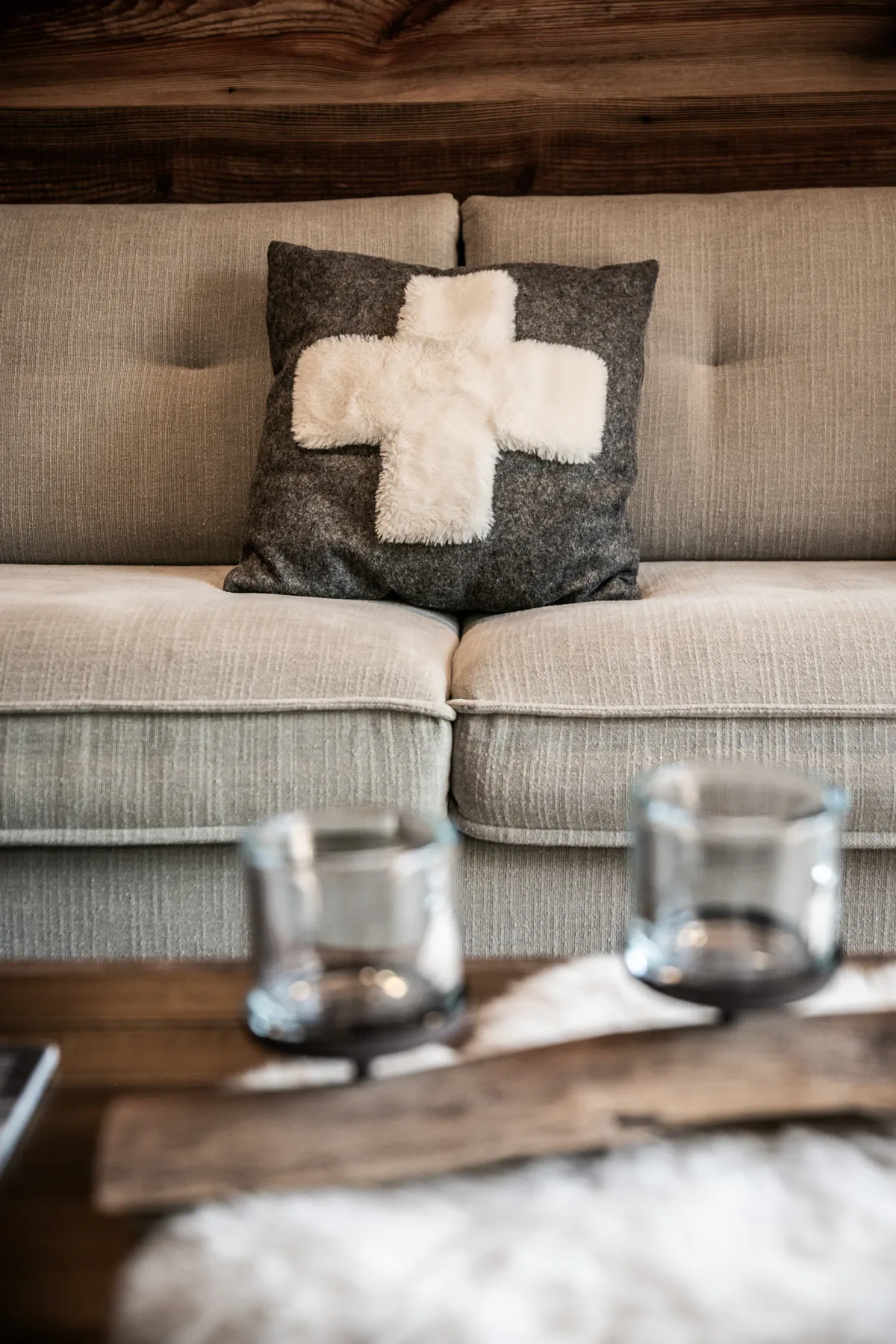 Un sofá beige con un cojín oscuro con una cruz blanca está detrás de una mesa de centro de madera.